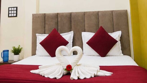 A hotel room with a bed, two wall sconces, a ceiling fan, and a decorative swan on the bed. - Gk Palace (Varanasi)