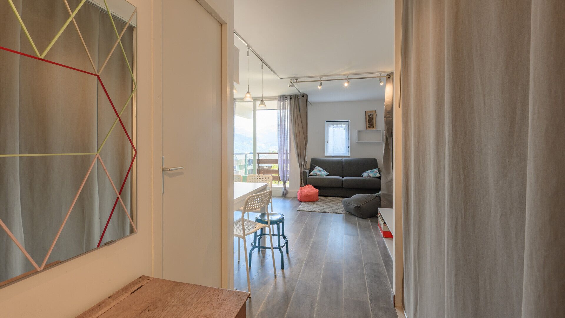 A modern living room with a sofa, a dining area with a table and chairs, and a view through a glass door.