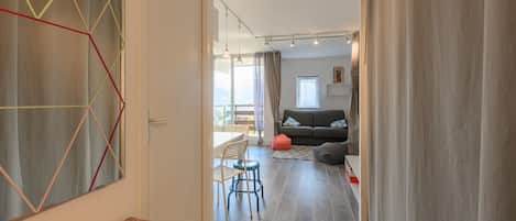 Ein modernes Wohnzimmer mit einer Couch, einem Essbereich mit Tisch und Stühlen und Blick durch eine Glastür.
