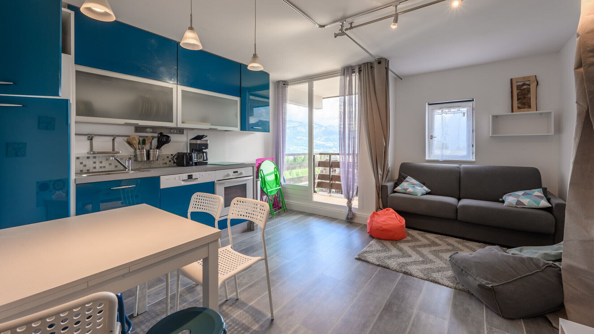 Una cocina moderna con armarios azules, una mesa de comedor y sillas. Hay un sofá y una ventana con vistas al exterior.