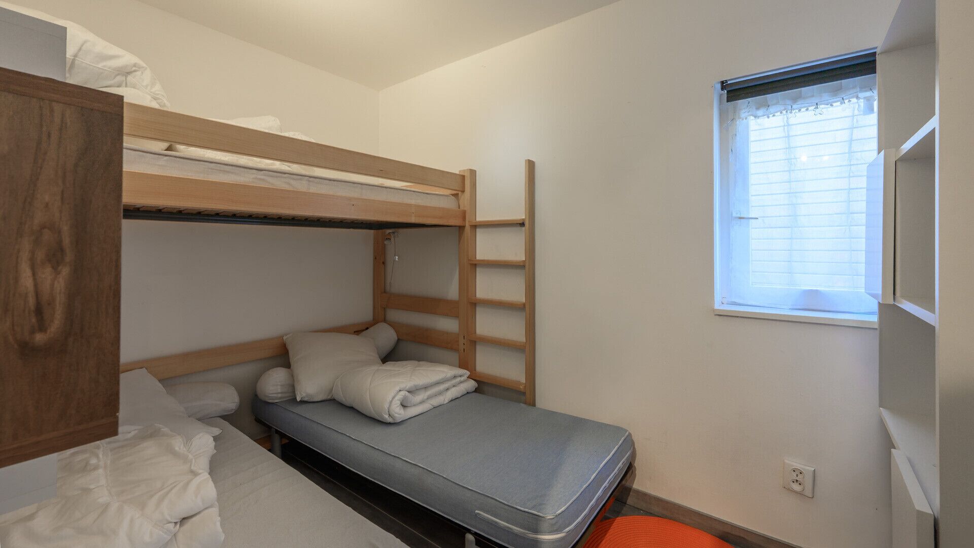 Une chambre de dortoir avec des lits superposés, un lit simple et une fenêtre avec des stores.