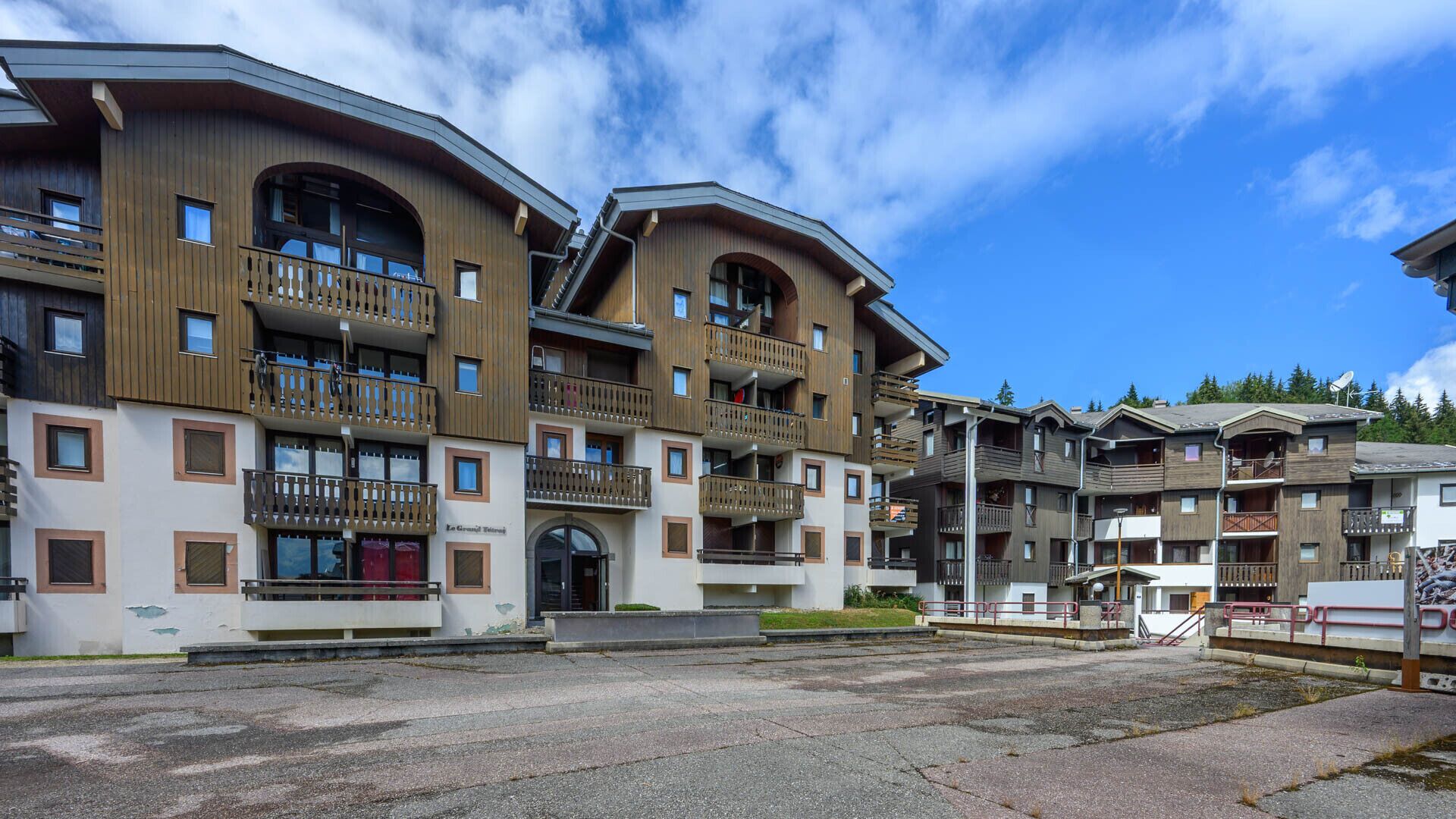 A multi-story hotel with balconies, a central entrance, and a parking area.