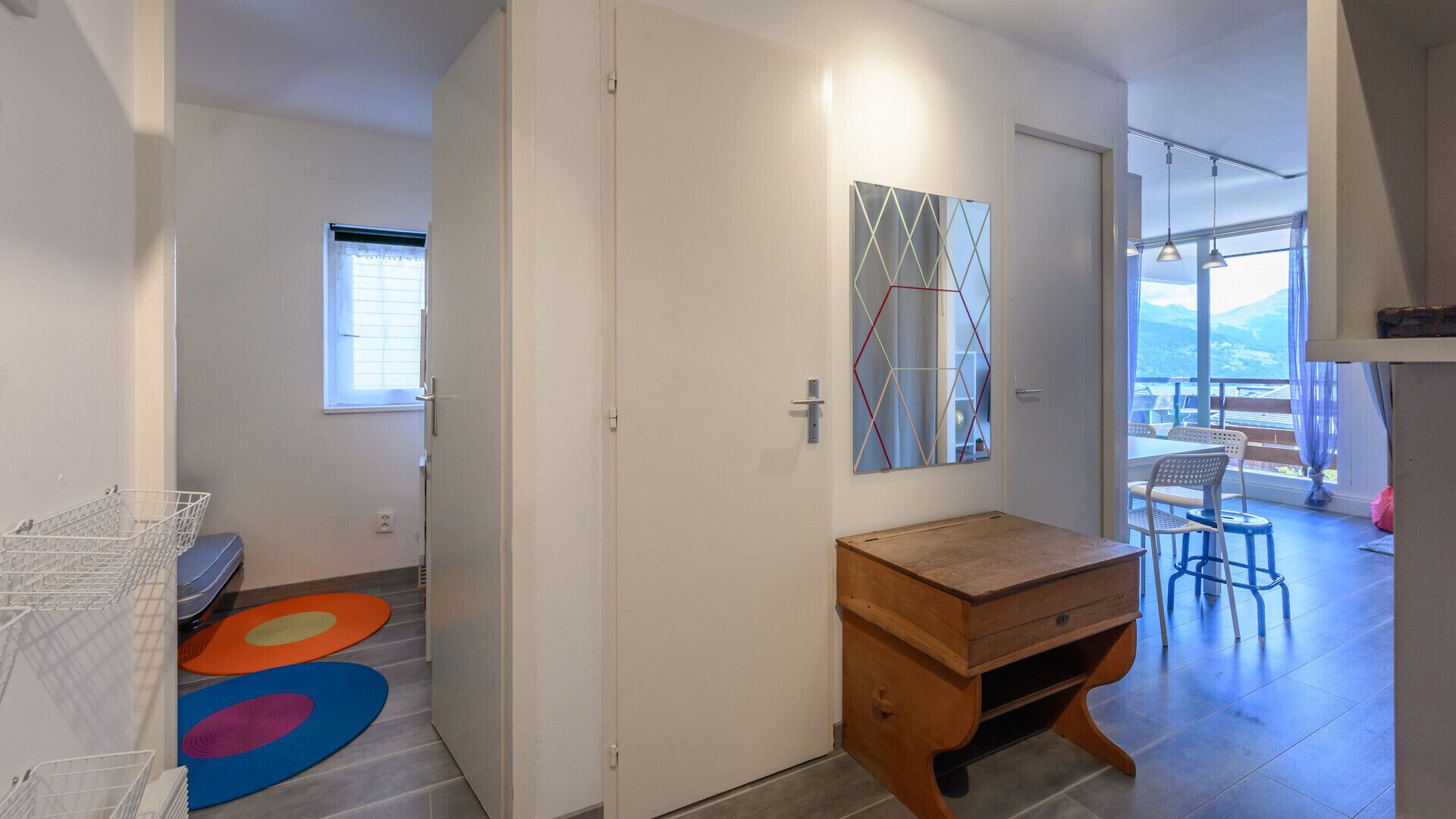 A hallway with a wooden desk, a colorful rug, and a large window with a view.