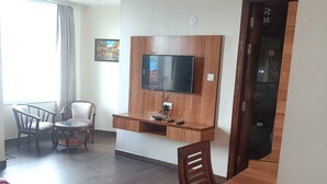 A hotel room with a bed, a desk, a chair, a TV mounted on a wooden panel, and a ceiling fan. - The Jade Mountain by O9 Stay (Banikhet)
