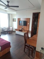 Habitación de hotel con una cama, un escritorio, una silla, un televisor fijado a un panel de madera y un ventilador de techo.