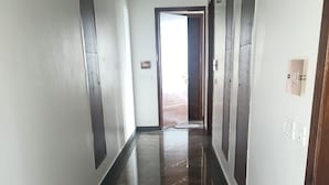 Un pasillo con piso brillante, puertas numeradas y una vista a otra habitación.