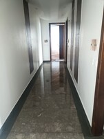 Un pasillo con piso brillante, puertas numeradas y una vista a otra habitación.