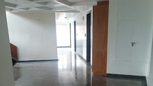 Un pasillo con piso pulido, paredes blancas y una puerta de madera.