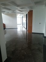 Un pasillo con piso pulido, paredes blancas y una puerta de madera.