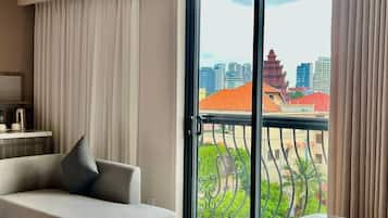 A modern hotel room with a sofa, a dining table, a large sliding glass door, and a view of a cityscape.