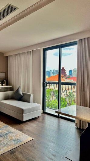 A modern hotel room with a sofa, a dining table, a large sliding glass door, and a view of a cityscape. - Lavia Hotel (Phnom Penh)
