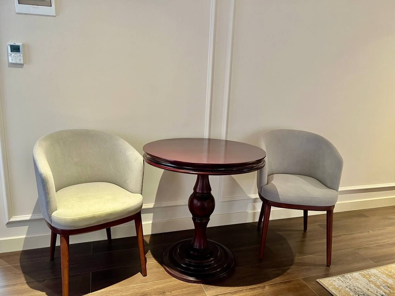 Een kamer met een ronde houten tafel en twee gestoffeerde stoelen.