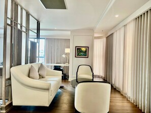 A modern living room with a sofa, armchair, and a coffee table. There is a painting on the wall and a window with curtains. - Lavia Hotel (Phnom Penh)