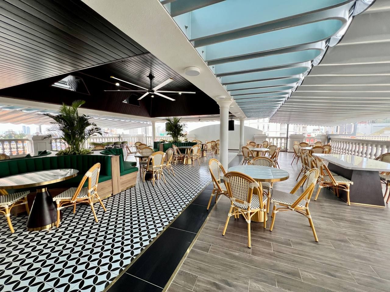 Un área de comedor en la azotea con mesas redondas, sillas de mimbre, piso estampado y techo de cristal.