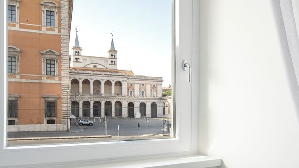 A room with a window overlooking a historic building, a small round table with breakfast items, and a newspaper.