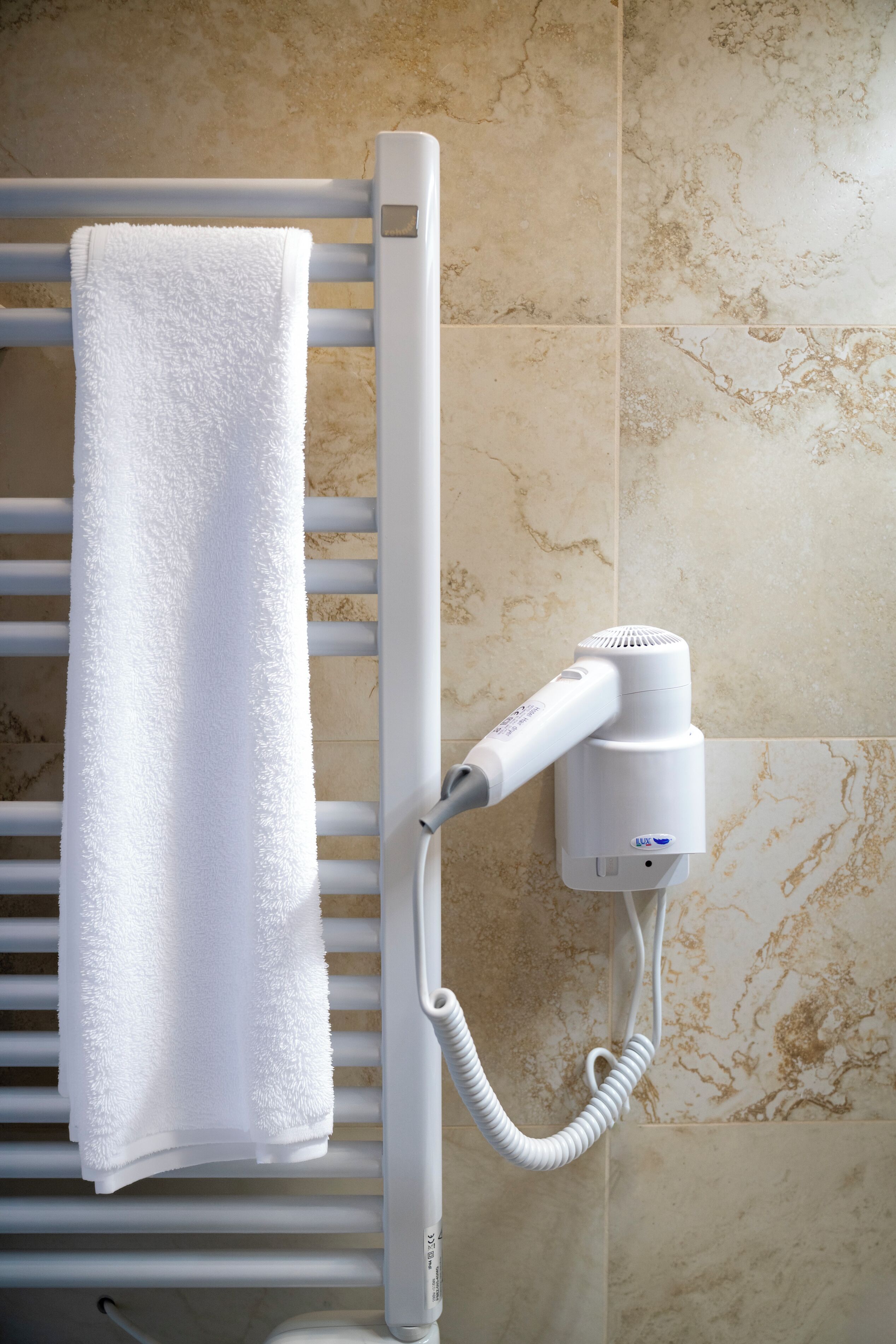 Een handdoek hangt aan een witte handdoekhouder in een badkamer met beige marmeren tegels.
