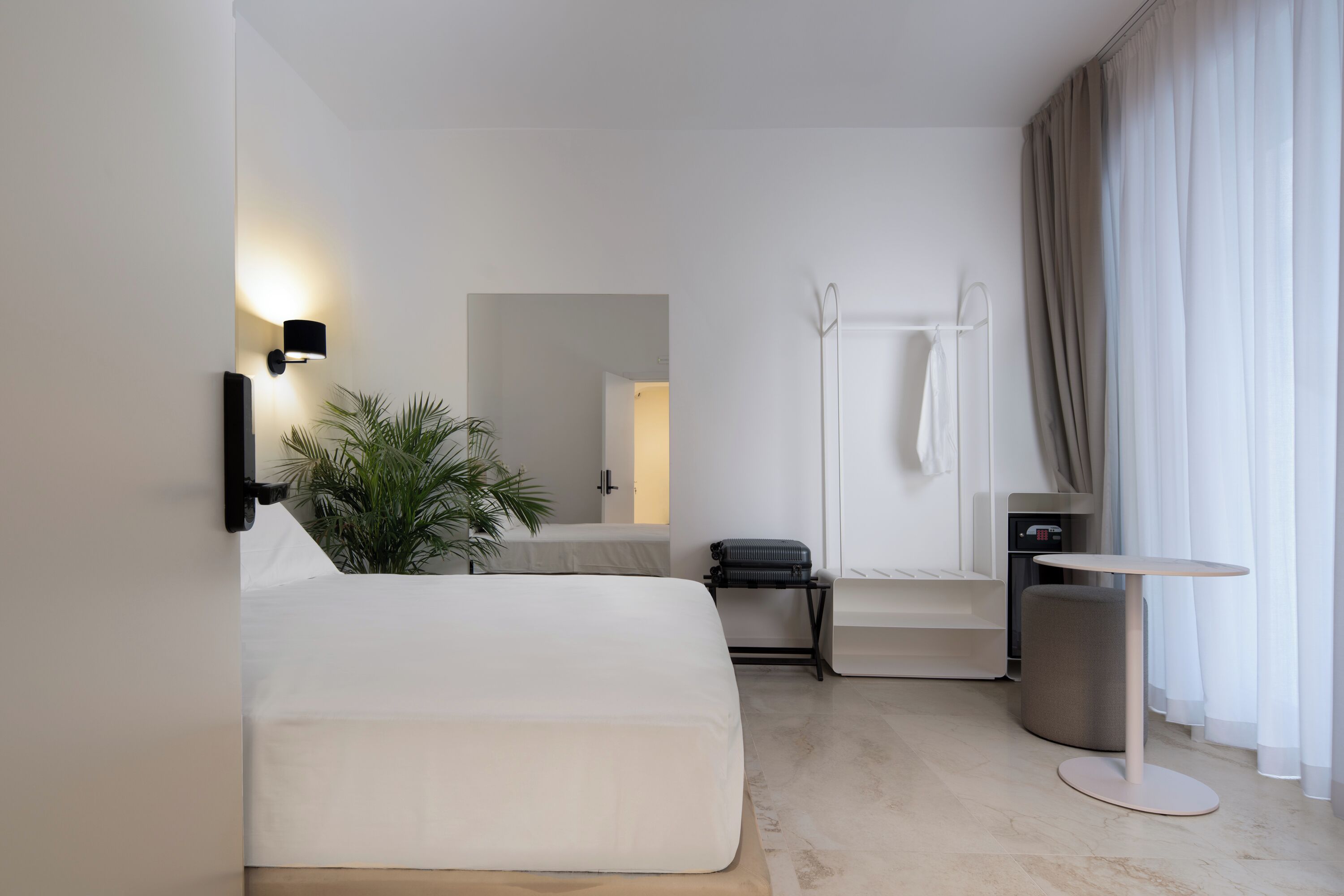 Habitación de hotel moderna con cama, mesita de noche, pequeño escritorio, zona de ducha y vistas al exterior.