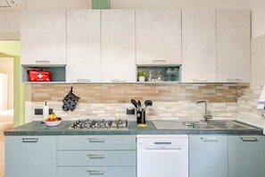 Eine moderne Küche mit einem Gasherd, einem Geschirrspüler und einer Spüle. Oberhalb der Arbeitsplatte befinden sich Schränke und auf dem linken Regal eine rote Kiste.