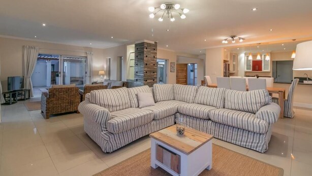 A modern living room with a sectional sofa, a coffee table, and a dining area with chairs. - Pezula Fairlead Luxury 7A  (Knysna)