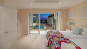 A hotel room with a bed, a nightstand, a lamp, and a view of a pool and sunset through a glass door. - Pezula Fairlead Luxury 7A  (Knysna)