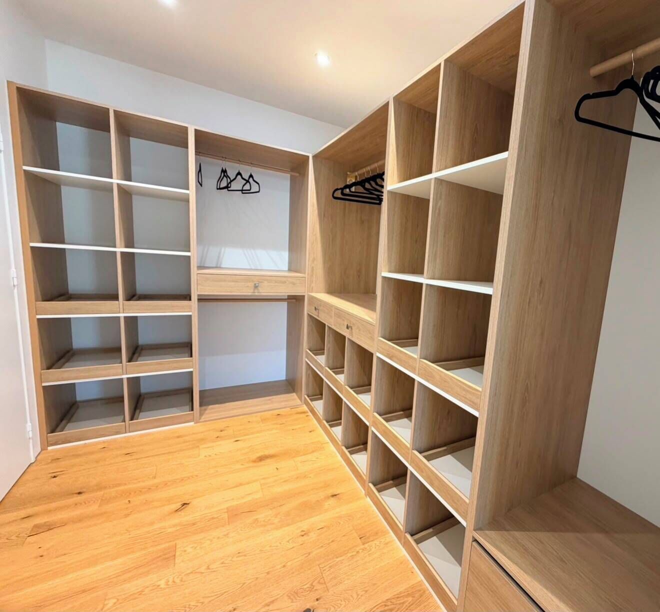 Un dressing avec de nombreuses étagères et un espace pour suspendre les vêtements, un plancher en bois et un mur blanc.