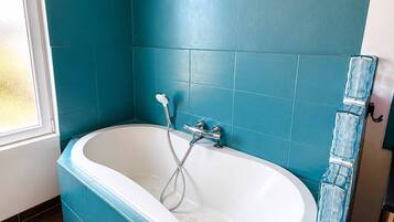 Une salle de bain avec une baignoire sur pieds, une pomme de douche et une étagère en verre pour la douche.
