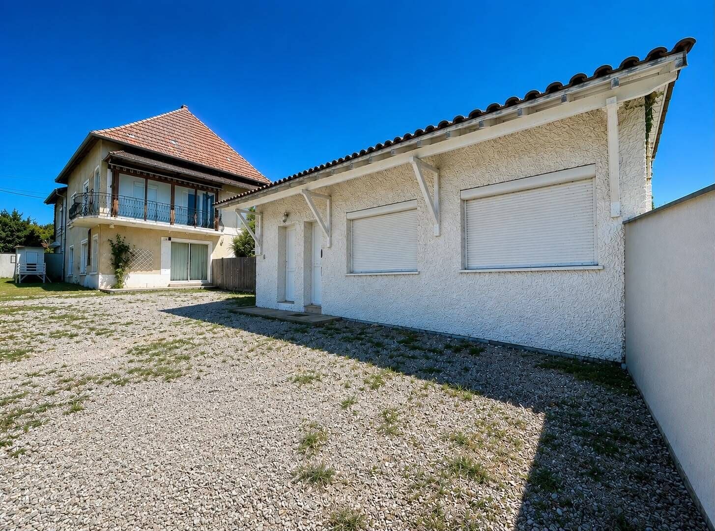 A two-story building with a tiled roof, a gravel driveway, and a white exterior wall.