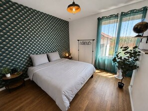 A bedroom with a patterned wall, a bed with white bedding, a bedside table with a lamp, a floor lamp, and a window with curtains.