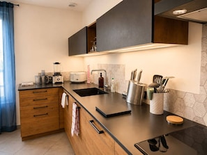 A modern kitchen with a black countertop, wooden cabinets, a built-in oven, and a stainless steel sink.