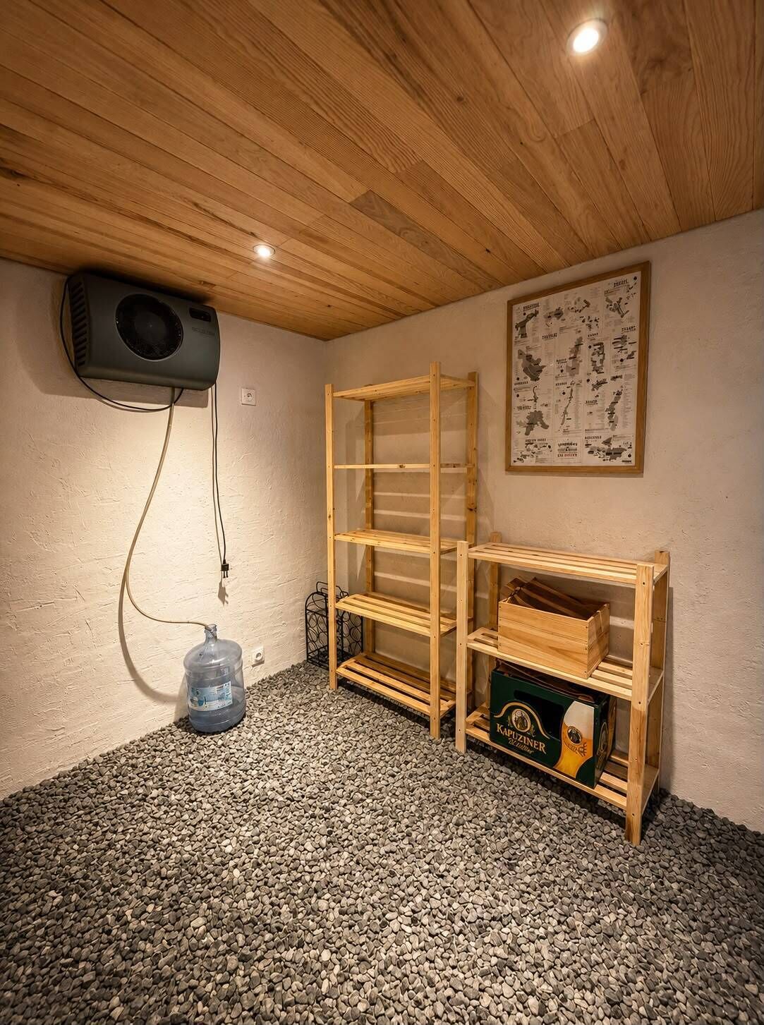 Una habitación con techo de madera, un proyector montado en la pared, una estantería de madera y un dispensador de agua en el suelo.
