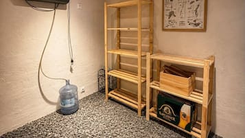 Una habitación con techo de madera, un proyector montado en la pared, una estantería de madera y un dispensador de agua en el suelo.