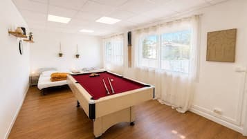 Una habitación con mesa de billar, cama y ventana con cortinas.
