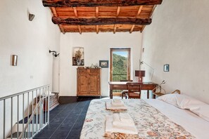 Ein Schlafzimmer mit einem Bett, einem Holztisch, einem Stuhl, einem Kleiderschrank und einem Balkon mit Blick auf Grünflächen.