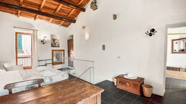 Ein Zimmer mit Holztisch, einem Bett mit floralem Überwurf und einer Treppe, sowie Blick ins Freie.