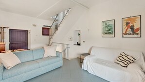 Ein Wohnzimmer mit einem blauen Sofa, einem weißen Sofa, einer Treppe und zwei Bildern an der Wand.