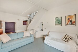 Ein Wohnzimmer mit einem blauen Sofa, einem weißen Sofa, einer Treppe und zwei Bildern an der Wand.