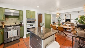 A modern kitchen with green cabinets, a stainless steel stove, and a dining area with a table and chairs.