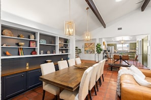 A spacious dining area with a wooden table and chairs, a kitchen in the background, and decorative shelves with various items.