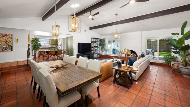 A spacious living area with a dining table, sofas, and a TV. There are ceiling fans and pendant lights.
