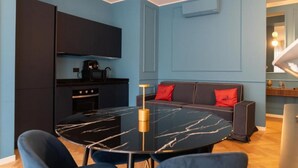 A modern living space with a round table, dark sofa, and a kitchen area. - VivimiHome-Suite Casa Degli Specchi (Milan)