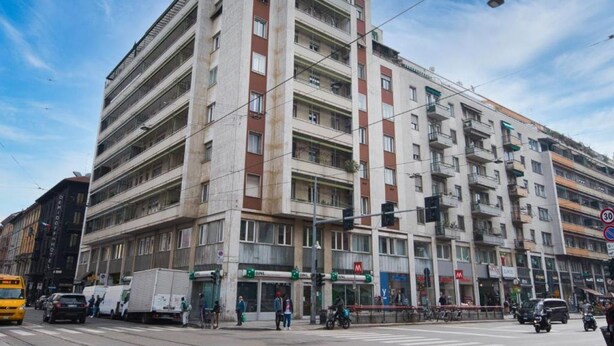 A multi-story building with commercial spaces on the ground floor, a traffic light, and a tram. - VivimiHome-Suite Casa Degli Specchi (Milan)