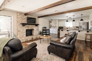 A living room with a stone fireplace, leather sofas, and a kitchen in the background. - The Getaway - Sleeps 12 (Belton)