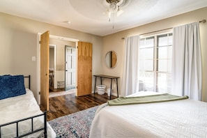 A bedroom with two beds, a wooden door, a small table, a mirror, and a window with curtains. - The Getaway - Sleeps 12 (Belton)