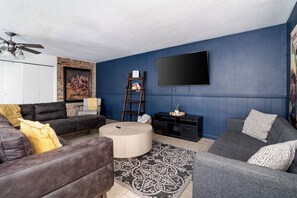 A living room with a blue wall, a mounted flat-screen TV, a ceiling fan, and a fireplace. - The Getaway - Sleeps 12 (Belton)