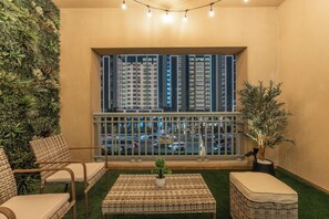 Ein Balkon mit Blick auf eine Stadtlandschaft, Korbmöbel und einem Blumentopf.