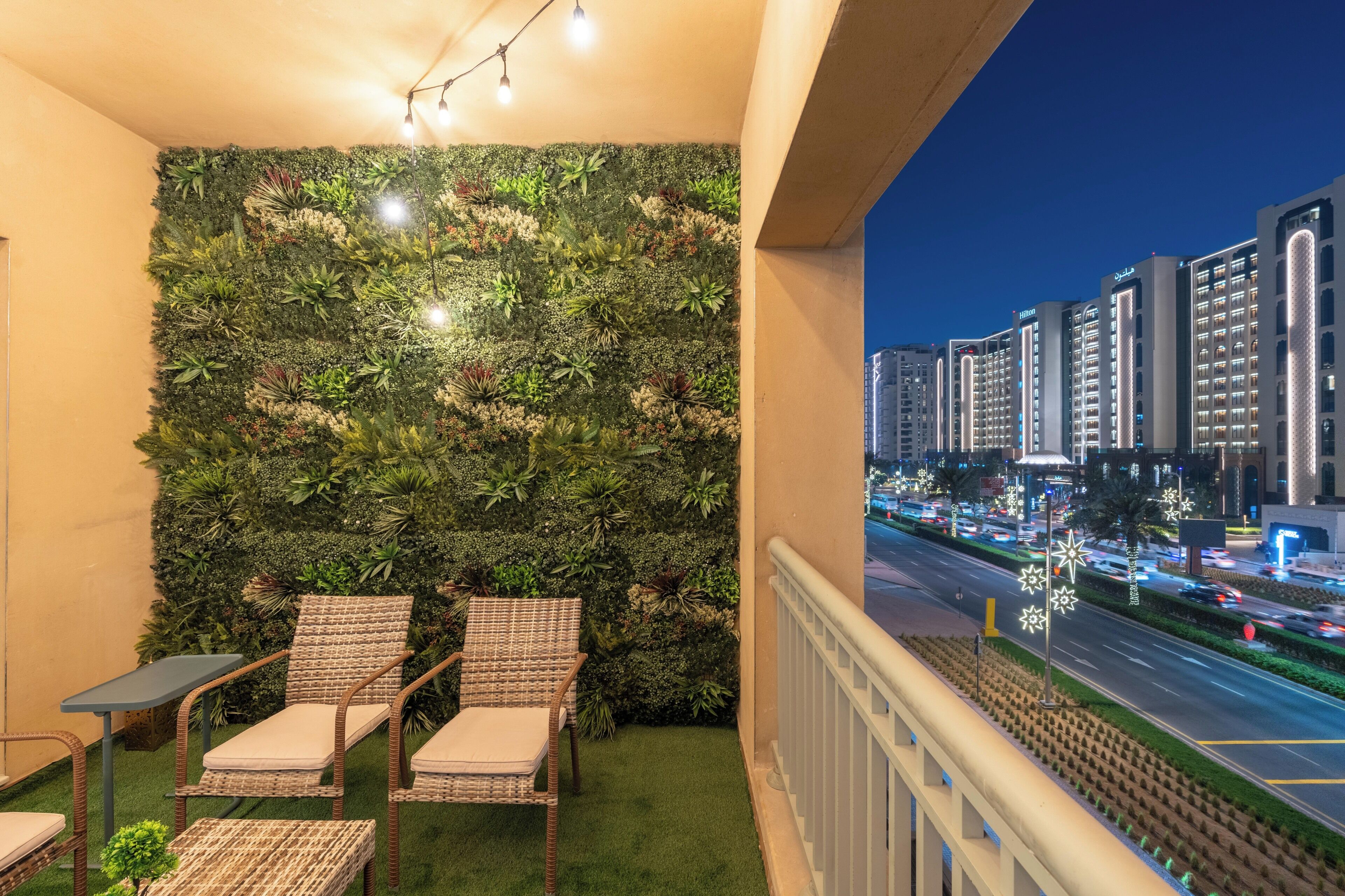 A balcony with a green wall, wicker chairs, and a view of a cityscape at night.