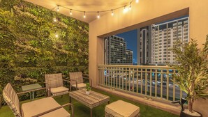 A balcony with wicker furniture, a green wall with plants, and a view of city buildings at night.