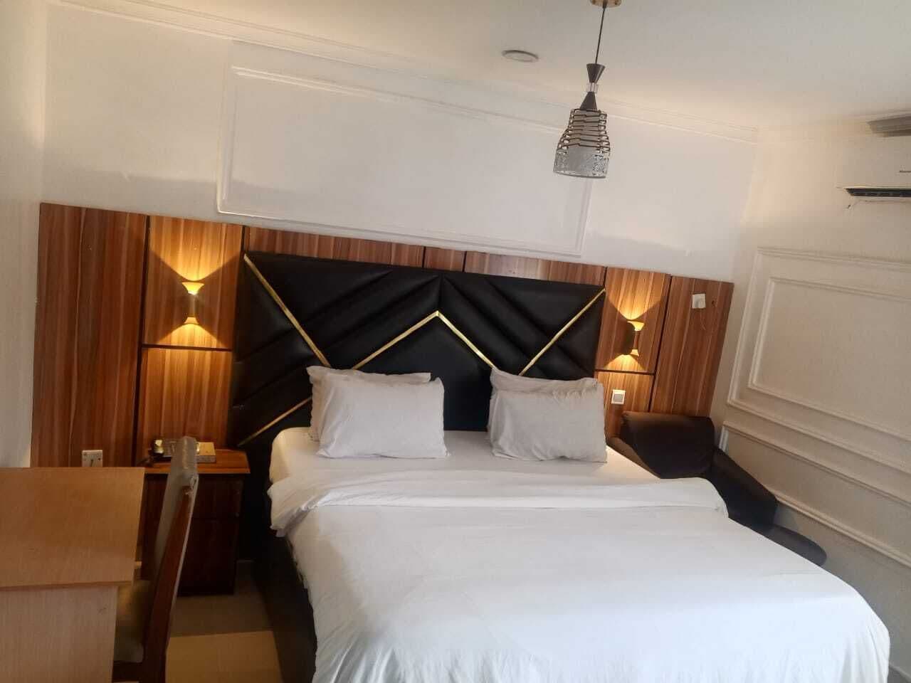 Una habitación de hotel con cama, mesitas de noche y lámparas de pared.