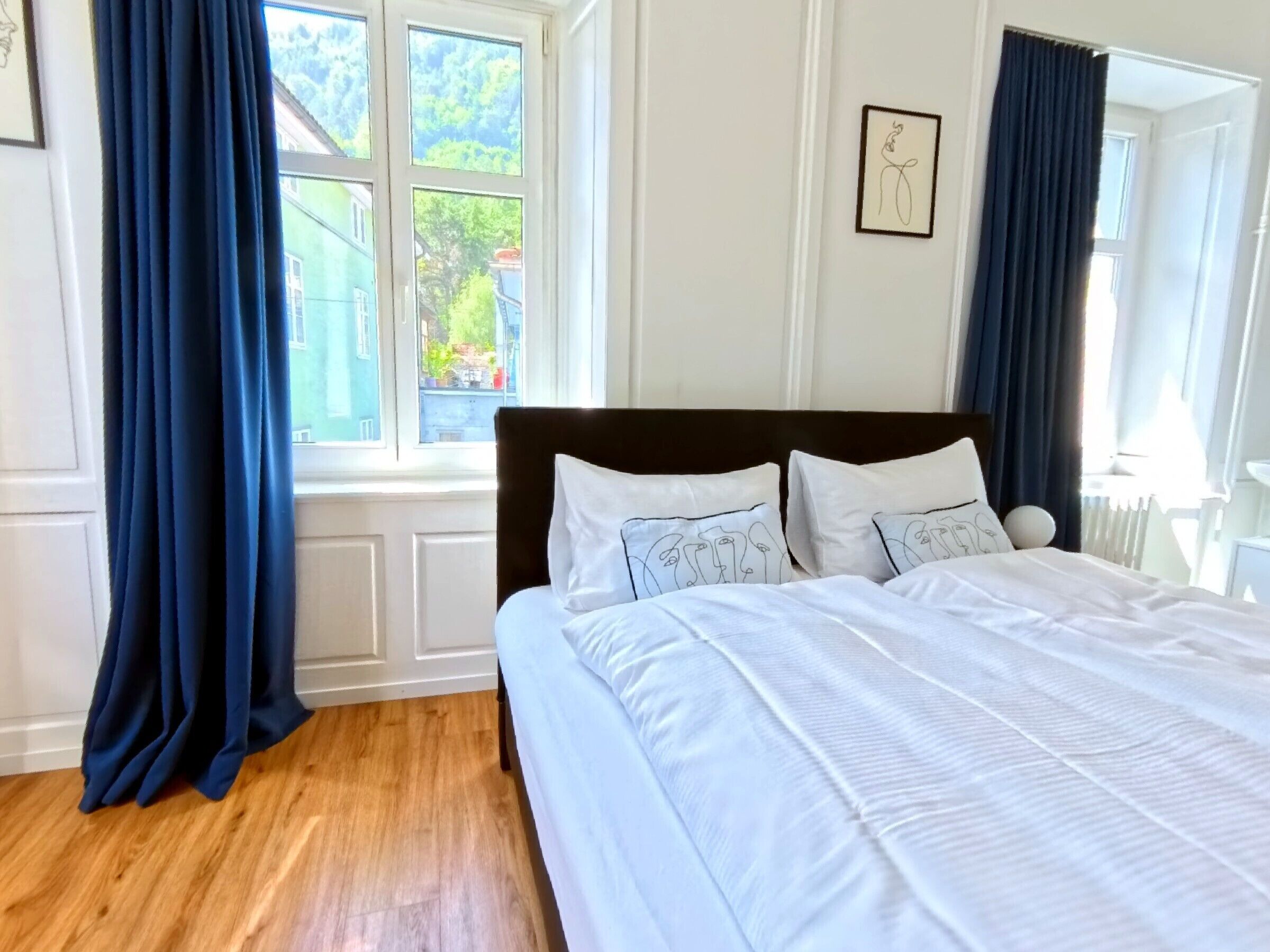 Un dormitorio con una cama grande, ropa de cama blanca y vistas al exterior con vegetación.