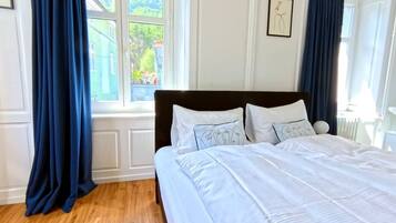 Un dormitorio con una cama grande, ropa de cama blanca y vistas al exterior con vegetación.
